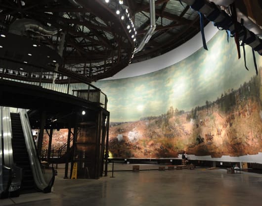 A museum visitor stands before a massive curved panoramic battle painting mounted inside a circular gallery.
