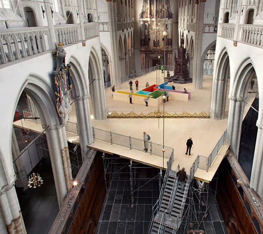 A raised plywood platform and colorful geometric installation built inside the nave of a Gothic church.