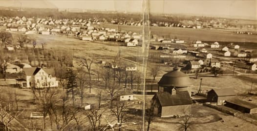 A grainy black-and-white aerial photo of the round barn surrounded by farmland and a scattering of houses.