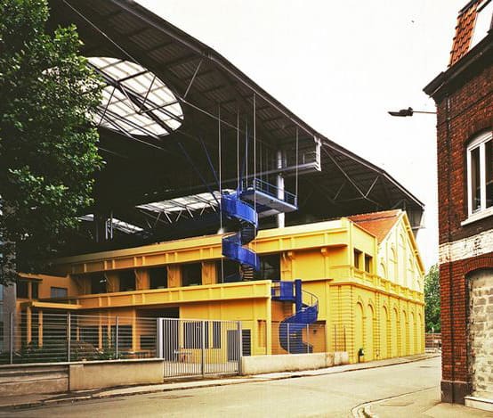 A yellow industrial building with a large umbrella-like roof canopy and exposed blue spiral stairs.