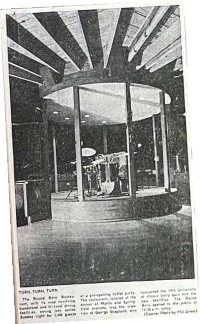 A newspaper clipping photo of a circular revolving bandstand stage inside the round barn's timber-ribbed interior.