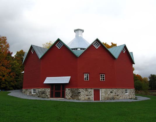 A red twelve-sided barn with a stone foundation and a white cupola, set in an open field.